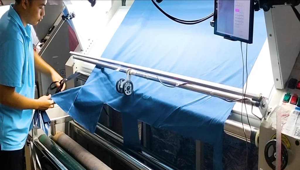 A worker inspecting fabric on a fabric inspection machine at a garment factory