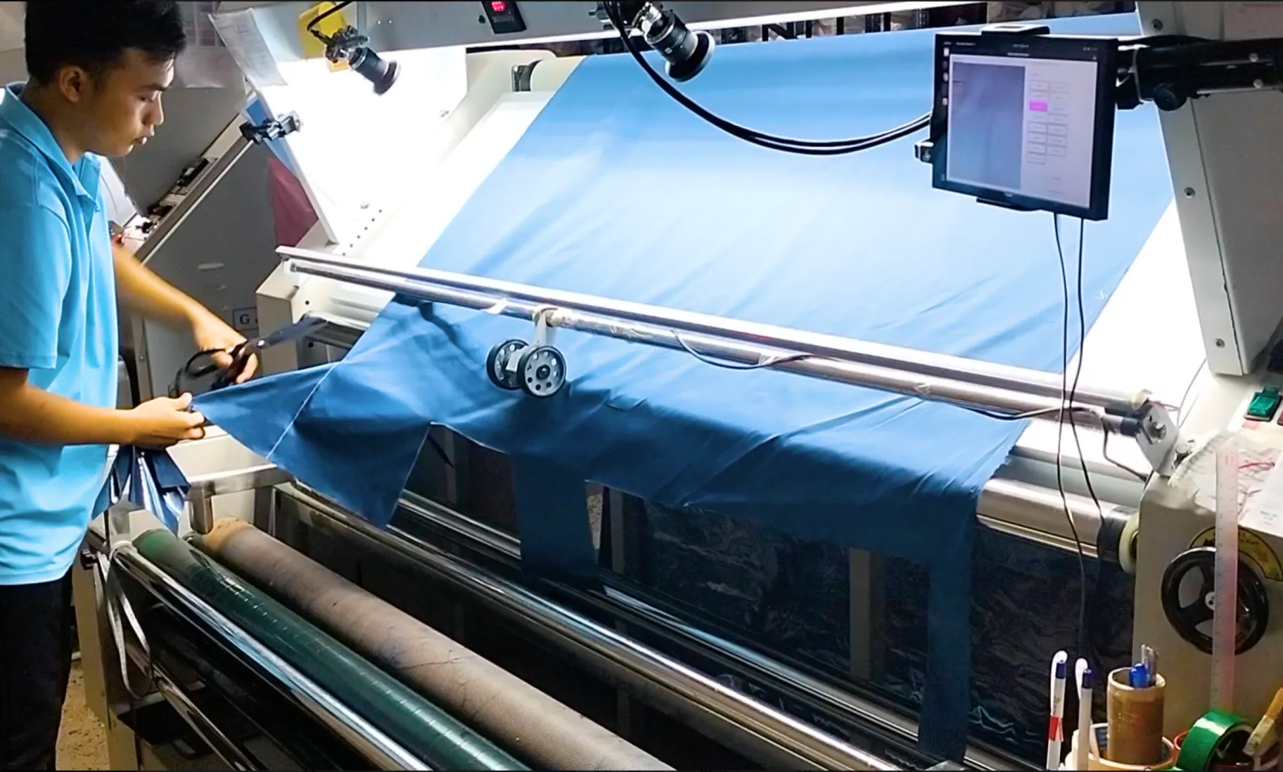 Worker operating a fabric inspection machine with an AI camera that detects defects automatically